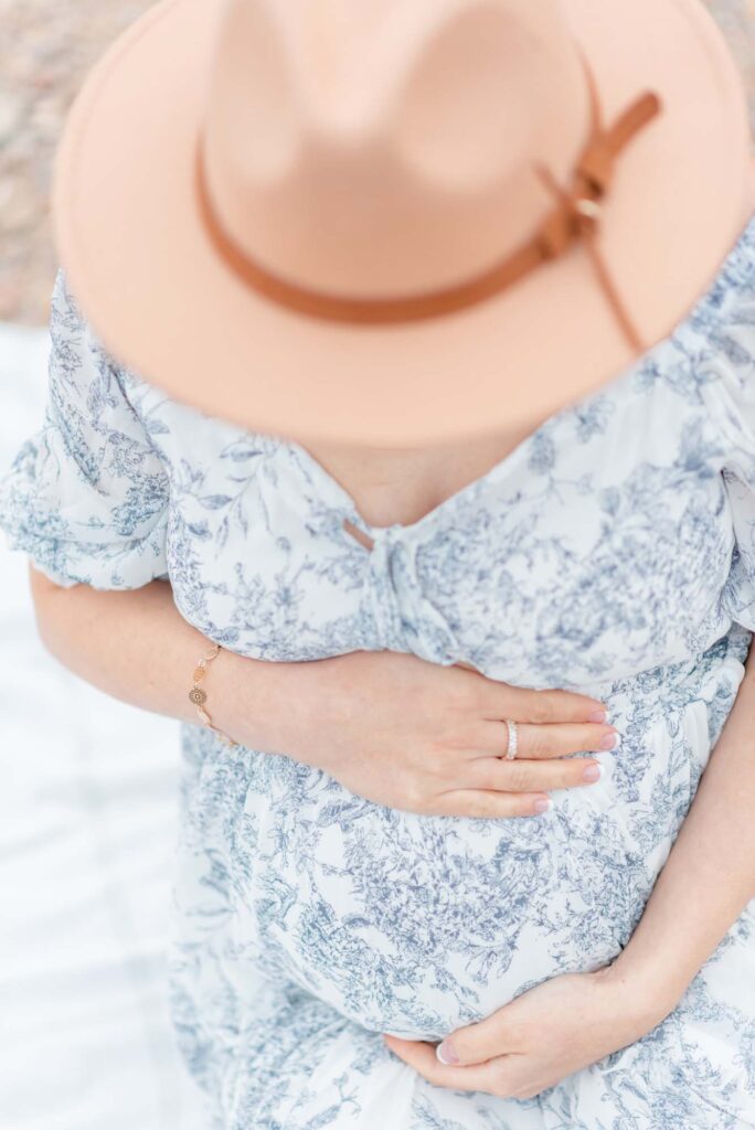 Expecting mom who is 32 weeks pregnant Wearing a white maxi dress with blue floral details and a tan fedora styled hat in the Desert in Tucson, Arizona for a maternity session.